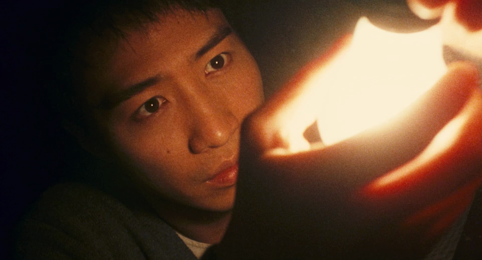 Still from Comrades: a young man lit by a warm light in his hands